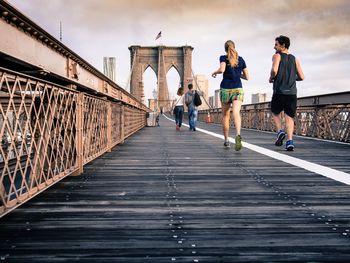 Rear view of people running on footbridge against sky