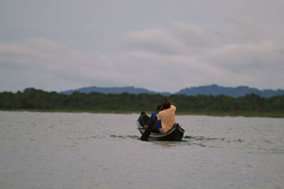 Men sitting in boat on lake against sky