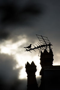 Low angle view of weather vane against cloudy sky