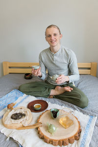 Happy man sitting on the bed, doing tea ceremony alone, stay home and be safe during carantine