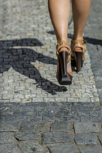 Low section of woman walking on cobblestone
