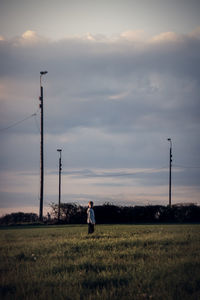 Boy standing on grassy field against cloudy sky during sunset