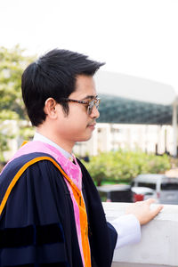 Mid adult man wearing graduation gown and sunglasses while standing outdoors