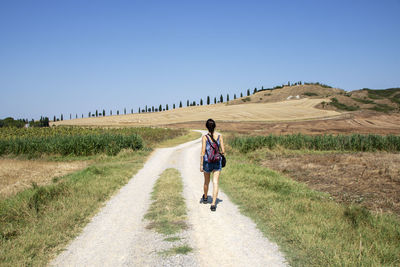 Rear view of woman riding bicycle on road against clear sky