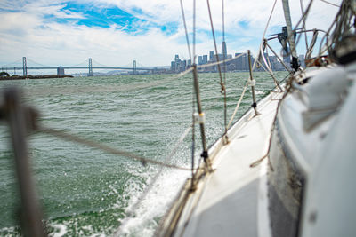 Sailboat sailing in sea against cityscape