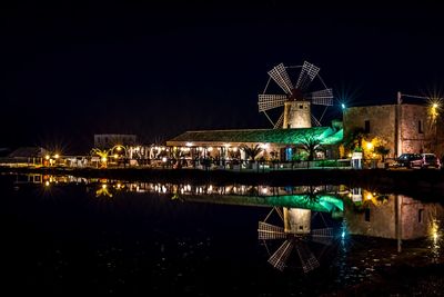 Illuminated ferris wheel in city against sky at night