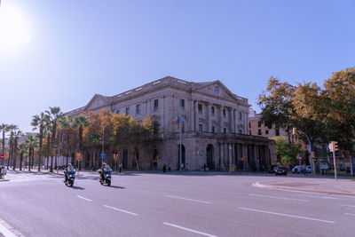 People on road by building against blue sky