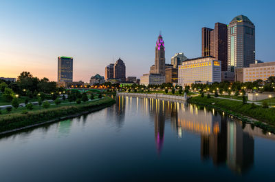 River by illuminated buildings against sky in city