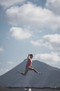 Woman with arms raised in mid-air against sky