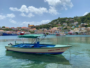 Sailboats moored in sea by town against sky