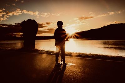 Rear view of silhouette man standing at beach during sunset