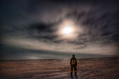 Rear view of man standing on beach against sky at sunset