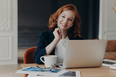 Portrait of smiling woman using laptop on desk in office