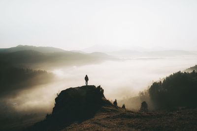 Rear view of man standing on mountain against sky during sunset