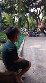 Side view of boy sitting on plant against trees