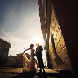 Bride and groom on street against cloudy sky on sunny day