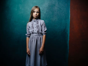 Portrait of a teenage girl standing against blue wall