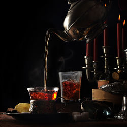 Teapot pouring tea in cup on table against black background