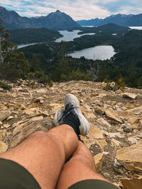 A man is laying on his back on a rocky hillside, with his legs crossed 