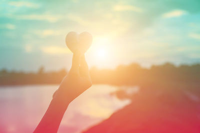 Close-up of silhouette hand holding sun during sunset