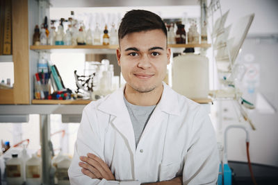 Portrait of smiling young male chemistry student standing with arms crossed in college laboratory