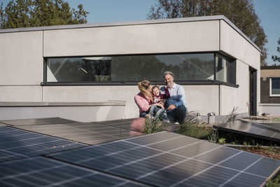 Happy girl with parents sitting by solar panel on rooftop