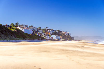 Scenic view of beach by town against clear blue sky