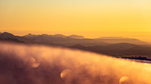 Scenic view of mountains and the orange sky reflect on the snow