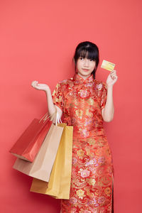 Smiling young woman holding red umbrella against orange background