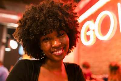 Smiling afro woman with neon lighting on face at bar