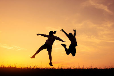 Silhouette people jumping on field against sky during sunset