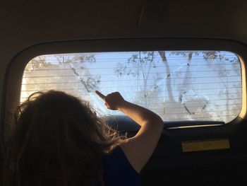 Rear view of girl drawing on frozen car window