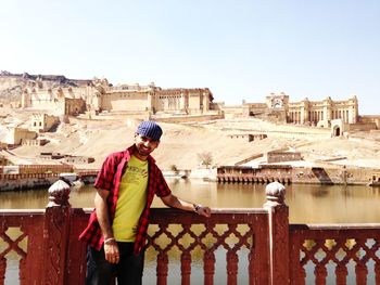 Young man standing at river by amber fort against sky