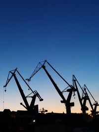 Low angle view of silhouette crane against clear blue sky