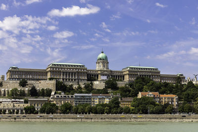 Buildings by river against cloudy sky