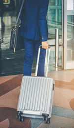 Midsection rear view of businessman with suitcase walking on floor at airport