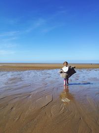 Rear view of girl with arms outstretched walking at beach against blue sky during sunny day