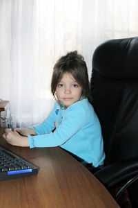 Portrait of girl sitting by desk at home