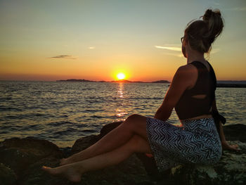 Woman sitting on beach at sunset