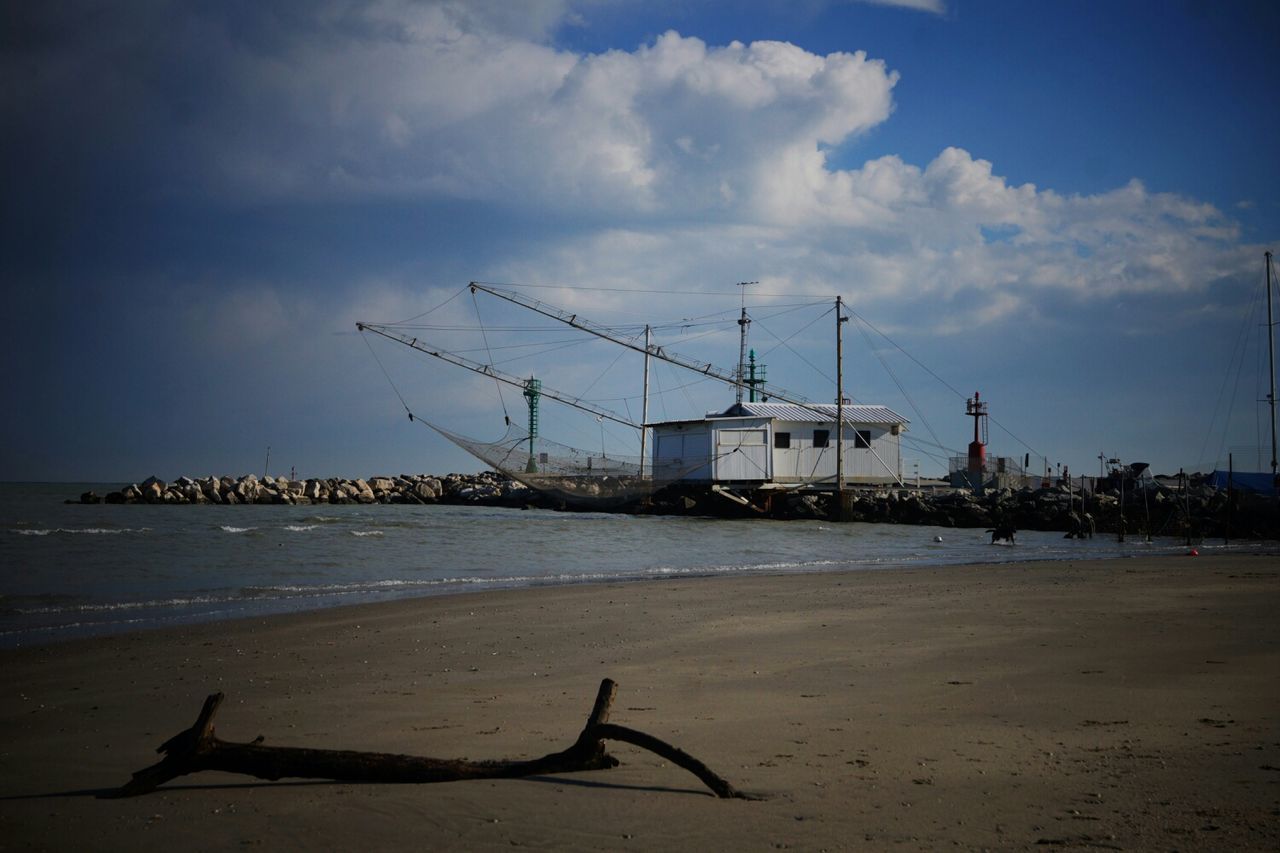 sky, built structure, architecture, building exterior, sea, water, beach, cloud - sky, sand, shore, crane - construction machinery, nautical vessel, transportation, cloud, harbor, bird, nature, outdoors, incidental people, day