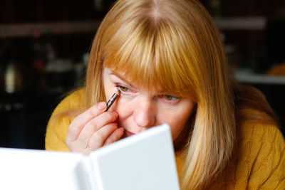 Blonde woman making up eyelashes herself with a hand mirror indoor. eyeliner makeup. attractive 