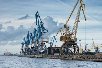 Cranes at commercial dock against sky