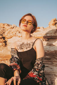 Woman sitting on rock against sky