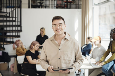 Portrait of smiling male programmer holding tablet pc while standing in office