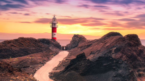 Lighthouse by sea against sky during sunset