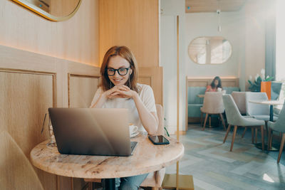 Young woman using laptop while sitting on sofa at home