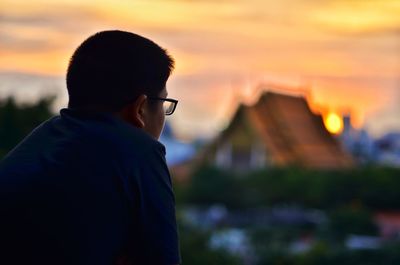 Young man looking away while sitting outdoors during sunset