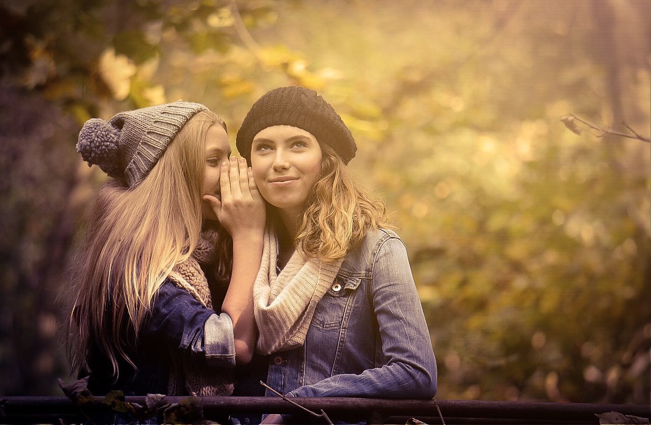 person, portrait, looking at camera, young adult, lifestyles, smiling, leisure activity, front view, focus on foreground, casual clothing, young women, three quarter length, happiness, standing, waist up, forest, sitting