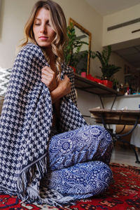 Woman wearing a crystal necklace meditation at home wrapped up in blanket