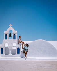 People walking in front of temple against clear blue sky